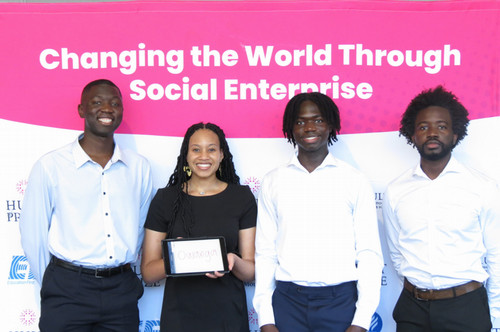 Four students stand before a banner reading "Changing the World Through Social Enterprise."